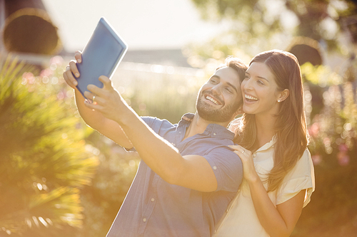 Smiling couple clicking selfie with digital tablet at park