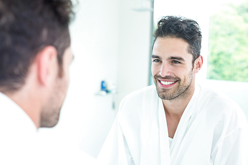 Happy handsome man looking in mirror at bathroom