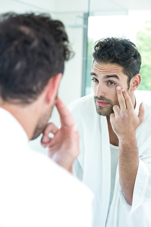 Handsome man checking eyes in bathroom mirror