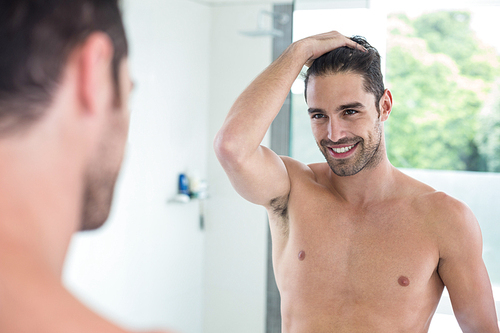 Handsome shirtless young man smiling while looking in mirror at bathroom