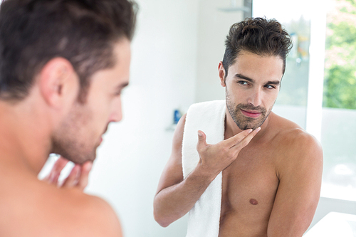 Smart young man looking in mirror at bathroom