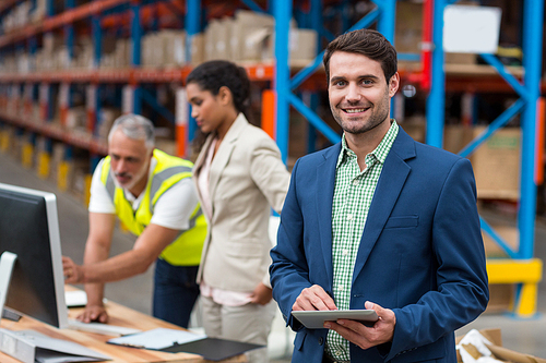 Focus on manager is smiling and holding a tablet in front of his colleagues in a warehouse