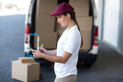 Portrait of delivery woman is writing something on a clipboard in front of a van
