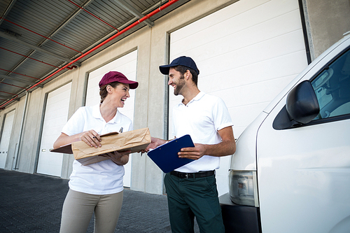 Low angle view of delivery people are looking each other and laughing in front of a warehouse
