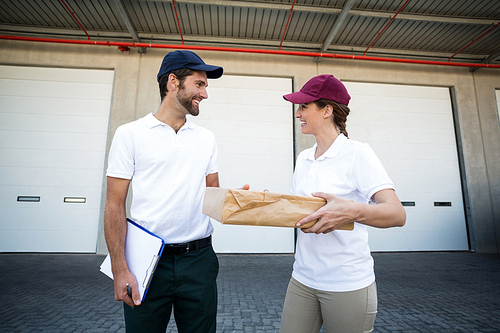 Portrait of delivery people are holding a cardboard box in front of a warehouse
