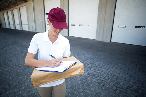 Portrait of delivery man is writing something on a clipboard in front of a warehouse