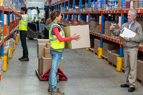 Manager looking a worker holding cardboard boxes with thumbs up in a warehouse