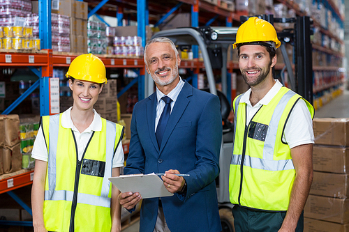 Manager and workers are posing and looking the camera in a warehouse