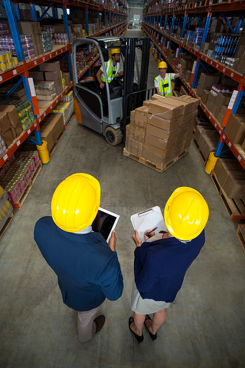 High angle view of manager wearing hard hat and looking workers in a warehouse