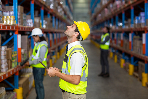 Worker with yellow safety vest looking up in warehouse