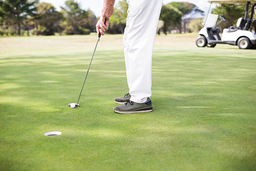 Low section of man playing golf while standing on field