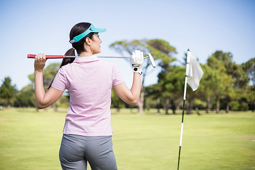 Rear view of woman holding golf club while standing on field