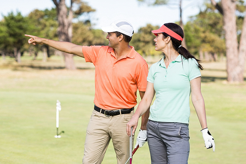 Smiling golfer man pointing while standing by woman on field