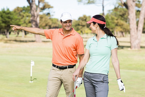 Cheerful golfer man pointing while standing by woman on field