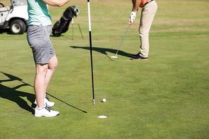 Low section of couple playing golf while standing on field