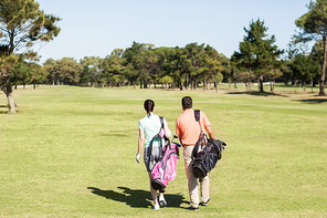 Rear view of couple carrying golf bags while walking on field