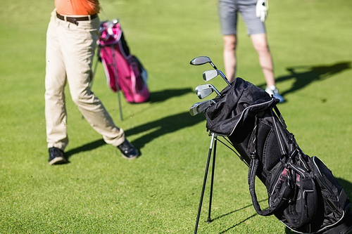 Low section of couple playing golf with bag on foreground