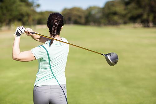 Rear view of golfer woman taking shot while standing at golf course