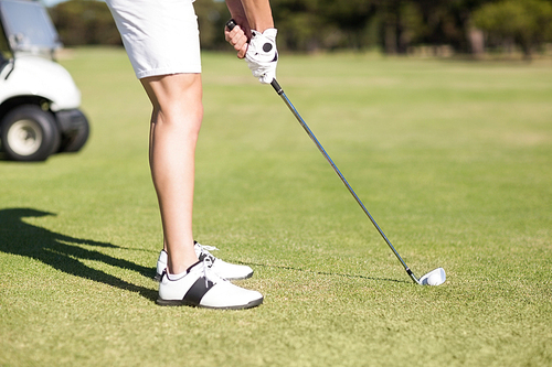 Low section of young man playing golf while standing on field