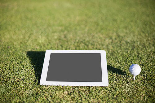 Close-up of golf ball on tee by digital tablet on field