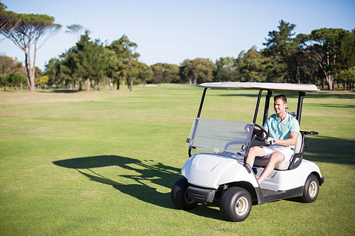 Full length of happy golfer man driving golf buggy on field