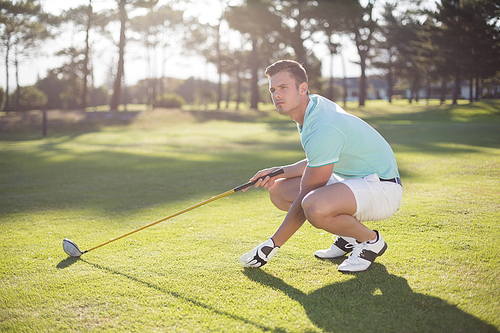 Full length of golfer man placing golf ball on tee while crouching at field