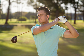 Handsome golfer man taking shot while standing on field