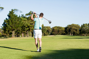 Rear view of young golfer man taking shot while standing on field