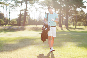 Young man looking at golf club while standing on field