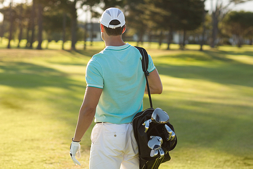 Rear view of golf player carrying bag while standing on field