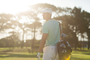 Rear view of golf player carrying bag while standing on field during sunny day