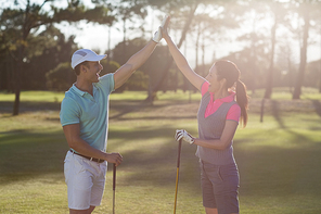 Smiling golf player couple giving high five while standing on field