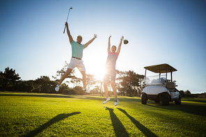 Full length of golf player couple with arms raised while jumping on field