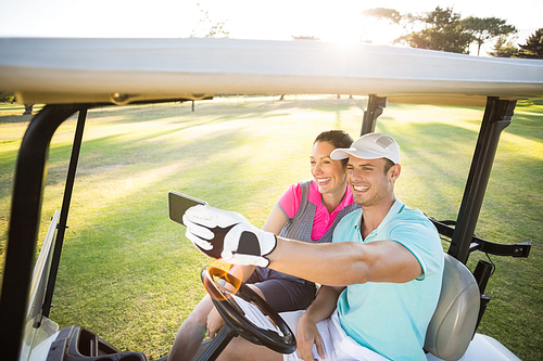 Smiling golfer couple taking selfie while sitting in golf buggy