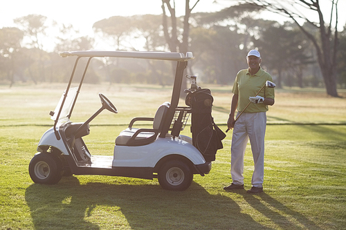 Portrait of smiling mature man standing by golf buggy on field