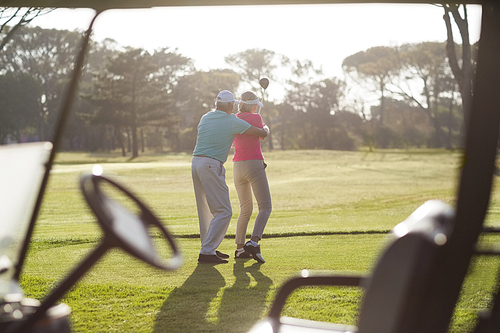 Rear view of mature man teaching woman to play golf while standing on field