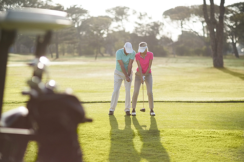 Full length of man teaching woman to play golf while standing on field