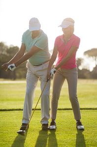 Full length of mature male golf player teaching woman while standing on field