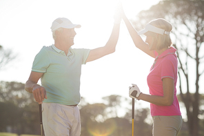 Happy golfer couple giving high five while standing on sunny day