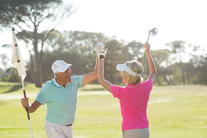 Cheerful mature golfer couple giving high five while standing on field