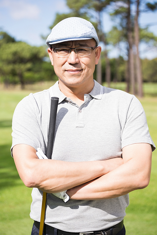 Portrait of happy golfer with arms crossed while standing at golf course