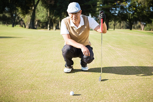 Golfer crouching and looking his ball on a field