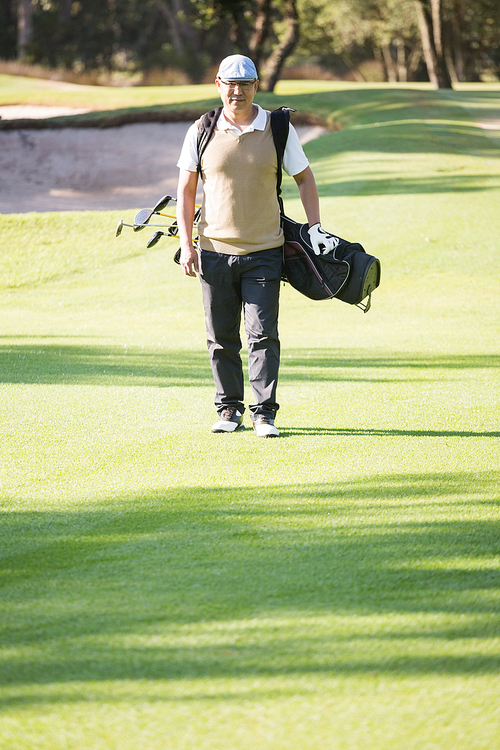 Portrait of sportsman walking with his golf bag on a field