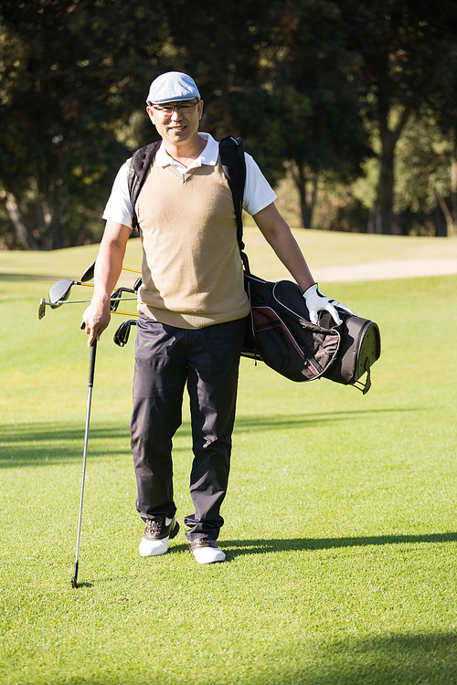 Sportsman posing with his golf bag on a field
