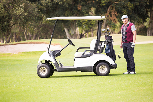 Golfer posing next to his golf buggy on a field