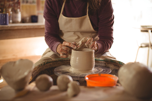 Mid section of male potter making pot in pottery workshop