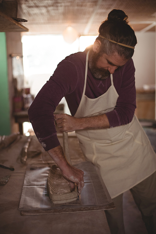 Male potter designing clay with stick in pottery workshop
