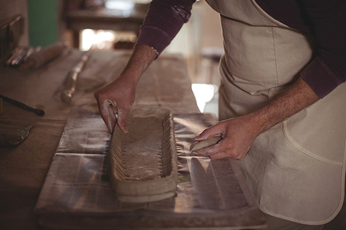 Mid section of male potter designing clay in pottery workshop