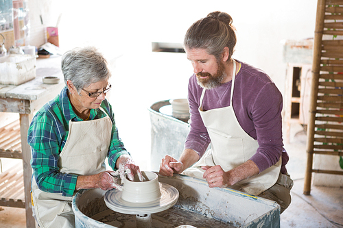 Male potter assisting female potter while making pot in pottery workshop