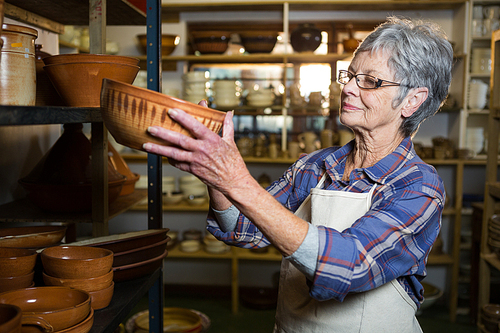 Female potter placing bowl on shelf in pottery workshop